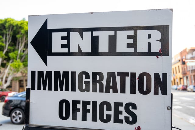 Directional sign reading "Enter Immigration Offices" with left arrow on city street parking area, San Francisco, California, August 14, 2025.