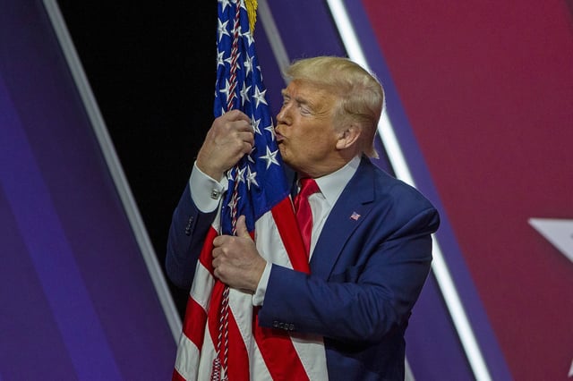 President Donald Trump kisses and hugs the flag of the United States of America at the 2020 CPAC convention.