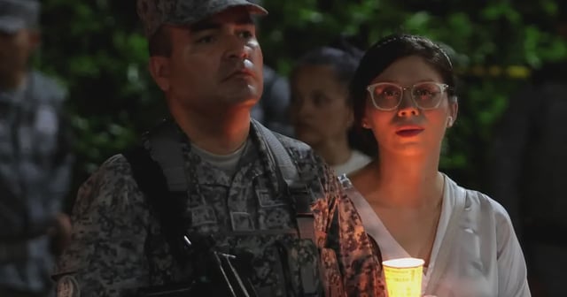 Mujer con blusa blanca sostiene una vela encendida junto a un soldado de la Fuerza Aérea Colombiana durante una vigilia nocturna en memoria de las víctimas del atentado con camión bomba ocurrido en Cali el 24 de agosto de 2025, que dejó seis muertos y más de 60 heridos.