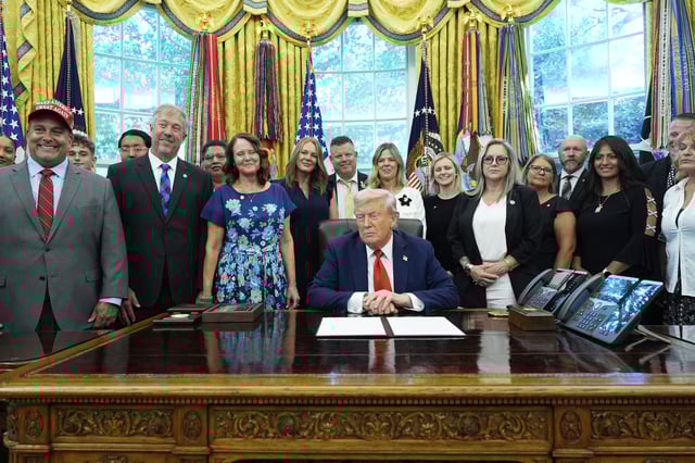 President Donald Trump, surrounded by family members of soldiers killed in Afghanistan at the attack at Abbey Gate, holds up a signed proclamation honoring the fourth anniversary of the attack, in the Oval Office of the White House, Monday, Aug. 25, 2025, in Washington. (AP Photo/Alex Brandon)