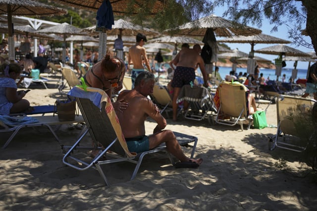 A woman applies sunscreen to a man at Avlaki beach about 42 kilometers (26 miles) east of Athens, Greece, Thursday, Aug. 7, 2025. (AP Photo/Thanassis Stavrakis)