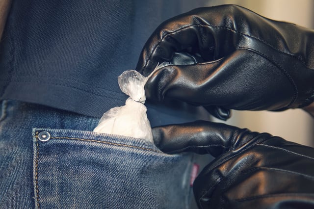 eine behandschuhte Hand zieht einen Beutel mit weißem Pulver aus der Gesäßstasche einer Jeans