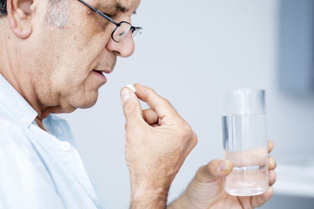 Mature pain taking painkiller pill with glass of water.