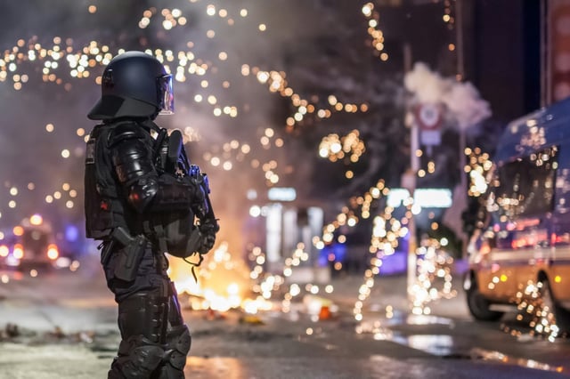 Fireworks explode near a police officer in riot gear in Lausanne