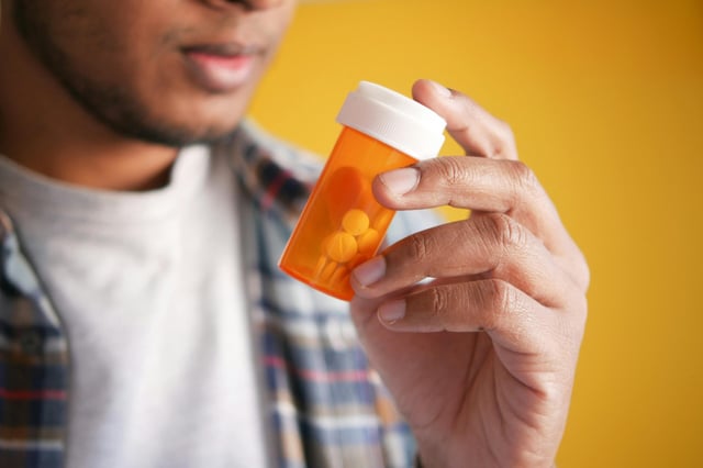 Close up of man holding an orange pill bottle