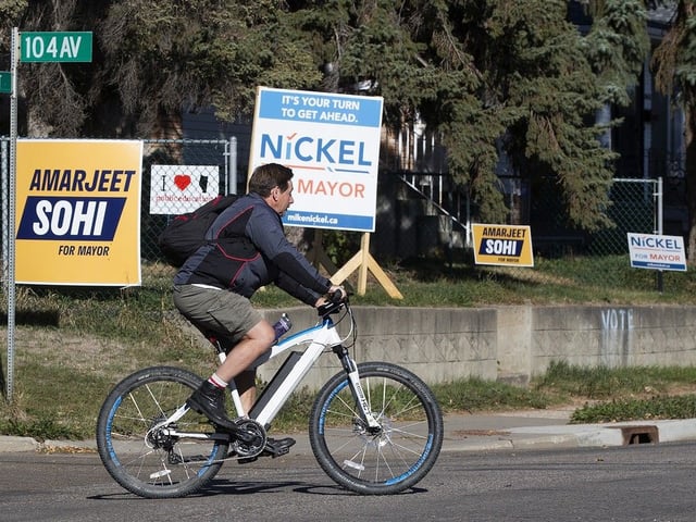 A cyclist makes their way past a home with both Amarjeet Sohi and Mike Nickel mayoral election signs in the front yard in Edmonton, on Oct. 4, 2021.
