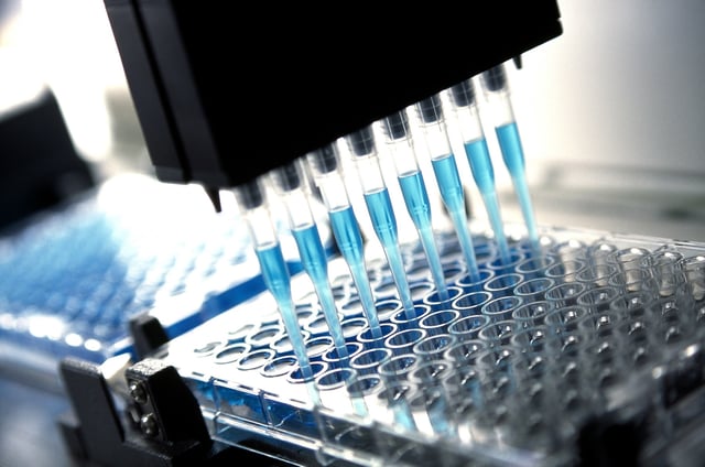 Robotic multichannel pipette device portions out blue fluid for medical and pharmaceutical research and testing. Close-up.