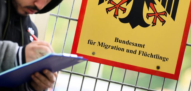 Ein Mann füllt ein Formular aus neben einem Schild des  Bundesamts für Migration und Flüchtlinge