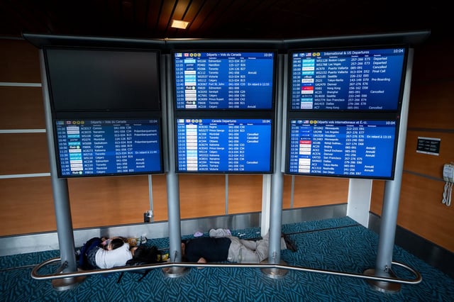 People sleep under a flight information board at the Vancouver International Airport in Richmond, B.C., Saturday, Aug. 16, 2025.THE CANADIAN PRESS/Ethan Cairns