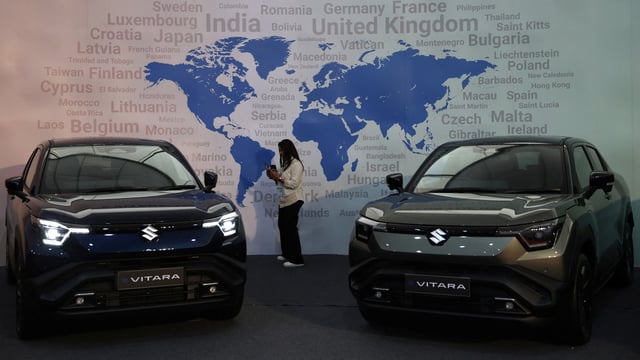 A visitor uses her phone next to Maruti Suzuki's e-Vitara SUV at the firm's Gujarat plant in Hansalpur Becharaji,.