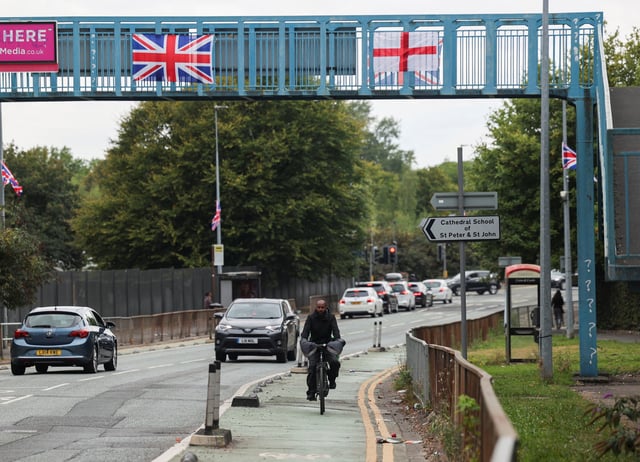 A Union Jack flag and England's flag of St. George hang on a pedestrian bridge as a cyclist and motorists drive by, in Salford, near Manchester, Britain August 22, 2025. REUTERS/Temilade Adelaja