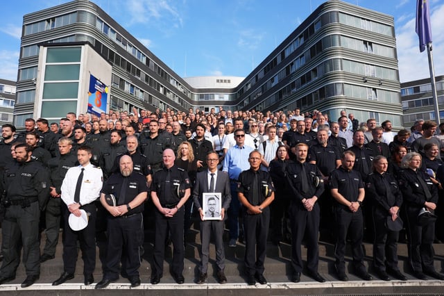 Hamburgs Polizeipräsident Falk Schnabel (vorne, M.), hält ein Foto des im Saarland getöteten Polizeioberkommissars Simon B. während einer Schweigeminute auf der Treppe vor dem Polizeipräsidium in Winterhude.
