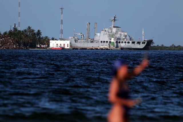 Hafenanalge, Person verschwommen im Vordergrund, dahinter eine Kriegsschiff, die Szenerie wirkt tropisch und lässt Venezuela vermuten