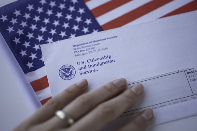 Stock photo shows a hand touching a USCIS letter resting on a U.S. flag.