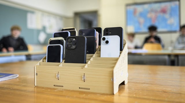 Mehrere Mobiltelefone stecken an einer Schule in einem Holzkasten.