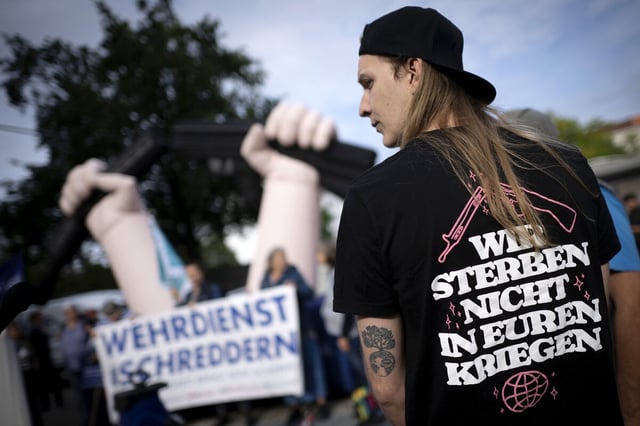 Ein junger mann trägt ein T-shirt; auf seinem Rücken stehen die Worte :"Wir sterben nicht in Euren Kriegen"