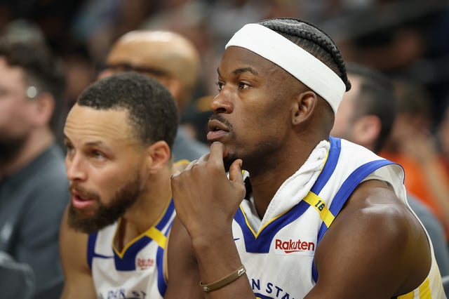 Jimmy Butler III #10 and Stephen Curry #30 of the Golden State Warriors watch from the bench during the second half of the NBA game against the Phoenix Suns at PHX Arena on April 08, 2025 in Phoenix, Arizona.