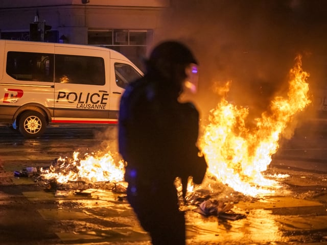 A police officer in riot gear walks past a fire in a street in Lausanne, on August 25, 2025, during a second night of rioting following the death of a teenager who tried to escape local police while driving a stolen scooter. (Photo by Fabrice COFFRINI / AFP) (Photo by FABRICE COFFRINI/AFP via Getty Images)