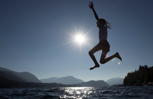 A young girl is silhouetted against the sun as she jumps in the waters of Sproat Lake in Port Alberni, B.C., on Tuesday, Aug. 31, 2018. THE CANADIAN PRESS/Jonathan Hayward