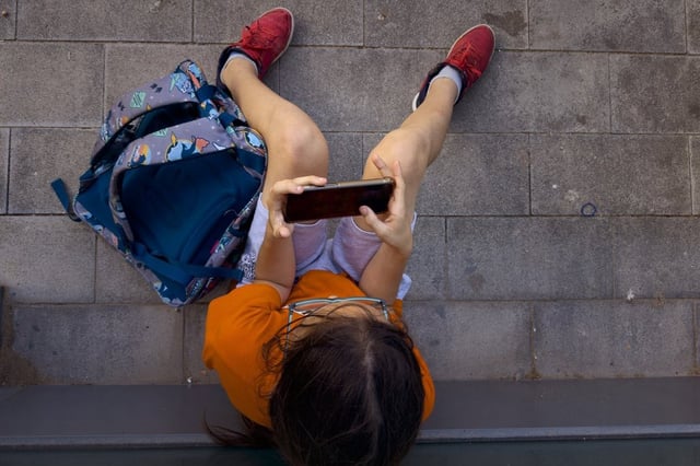 A boy plays on his father's phone outside a school in Barcelona, Spain, Monday, June 17, 2024. THE CANADIAN PRESS/AP-Emilio Morenatti