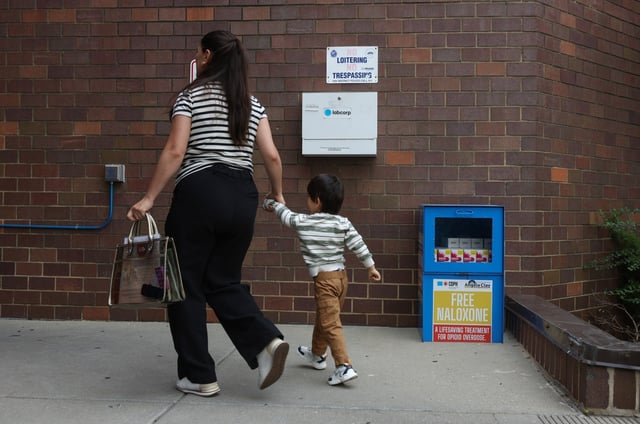 A woman and child walk past a newspaper box containing free doses of Narcan is placed near the front entrance of the Department of Family & Support Services (DFSS) location, 845 W. Wilson Ave., during the Harm Reduction Fair, Aug. 27, 2025, in Chicago. (John J. Kim/Chicago Tribune)