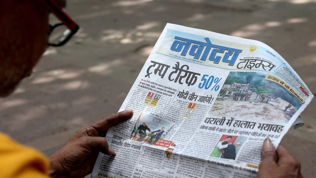 A man reads a newspaper with reports on tariffs after US President Donald Trump announced an additional 25% tariff on Indian goods