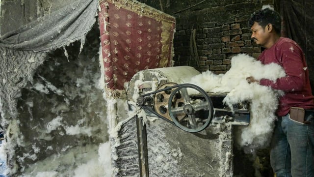 A worker feeds raw cotton into an opener machine at a processing facility in Amritsar 