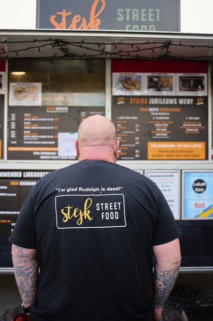 Zebastian Bohman, a co-owner of Stejk Street Food, wears a t-shirt that reads "I'm glad Rudolph is dead", standing outside his food truck in Kiruna, Sweden, Sunday, Aug. 17, 2025. (AP Photo/Malin Haarala)