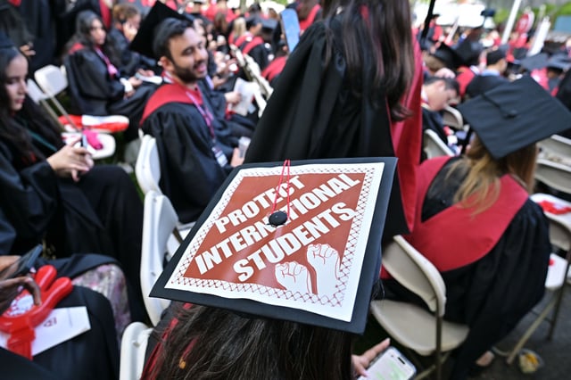 CAMBRIDGE, MA - MAY 29:  A Harvard University graduate with a message in support of international students on her mortarboard sits with fellow students at the start of commencement exercises at Harvard University in Harvard Yard May 29, 2025, in Cambridge, MA. (Photo by Josh Reynolds/For The Washington Post via Getty Images)