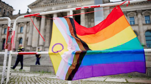Eine Regenbogenfahne hängt an einer Absperrung vor dem Reichstagsgebäude in Berlin.