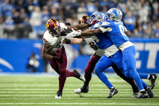 DETROIT, MICHIGAN - JANUARY 18: Brian Robinson Jr. #8 of the Washington Commanders runs in action against Alex Anzalone #34 and Terrion Arnold #0 of the Detroit Lions in the NFC Divisional Playoff at Ford Field on January 18, 2025 in Detroit, Michigan. (Photo by Nic Antaya/Getty Images)