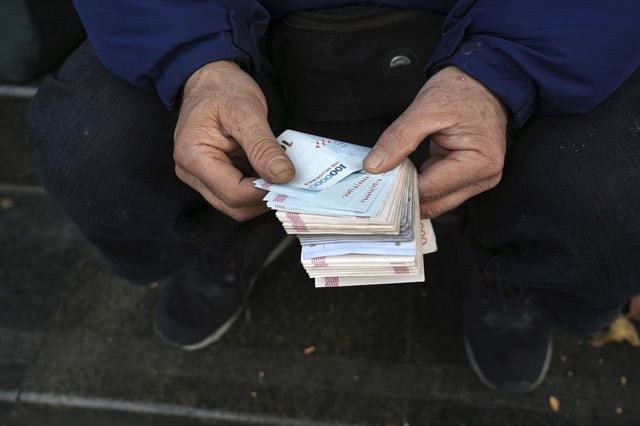 FILE - A street money exchanger poses for a photo without showing his face as he counts Iranian banknotes at a commercial district in downtown Tehran, Iran, Friday, Dec. 23, 2022. (AP Photo/Vahid Salemi, File)
