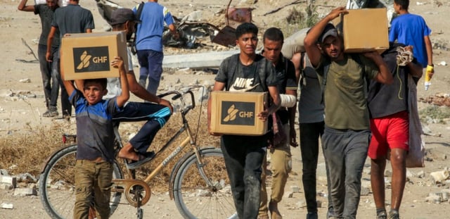 Des Palestiniens portent des cartons d'aide humanitaire reçus dans un centre de distribution géré par la Fondation humanitaire de Gaza (GHF), alors qu'ils traversent le "corridor de Netzarim", dans le centre de la bande de Gaza, le 22 août 2025