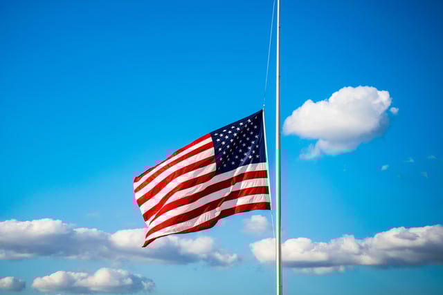 Stock photo shows the Stars and Stripes lowered to half-staff.