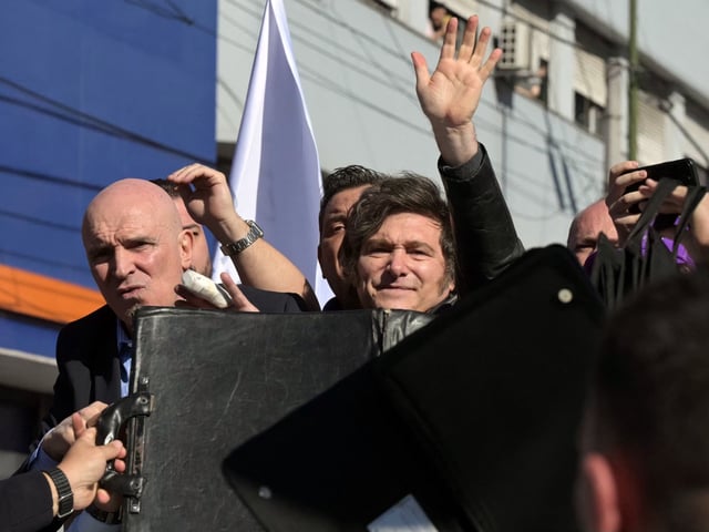 Bodyguards protect Argentina's President Javier Milei (C), his sister, Secretary General of the Presidency Karina Milei (unseen), the ruling party's candidate for deputy, Jose Luis Espert (L), and other officials and candidates as protesters throw objects at them during a motorcade in Lomas de Zamora, Buenos Aires province, Argentina, on August 27, 2025. Argentine President Javier Milei was evacuated from a campaign event on the southern outskirts of Buenos Aires after protesters threw objects at the vehicle in which he was traveling, amid controversy over an alleged corruption case involving the government. (Photo by Juan Mabromata / AFP)