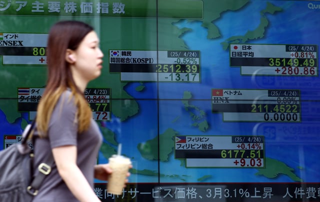 A woman walks past an electronic screen displaying the stock index prices of Asian countries outside a brokerage in Tokyo, Japan April 24, 2025. REUTERS/Issei Kato/ File Photo