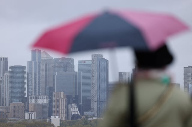 A woman holds an umbrella in view of the Canary Wharf skyline, London, Britain, October 28, 2024. REUTERS/Hollie Adams/File Photo