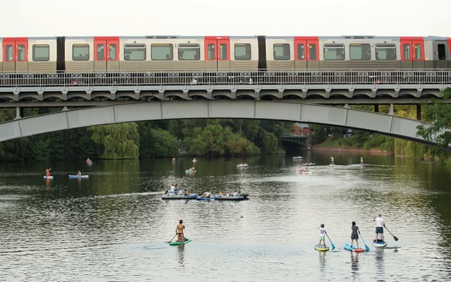 Passanten paddeln auf Stand-up Paddle Boards auf einem Alsterkanal unter einer Brücke entlang.