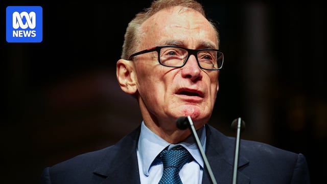 A man wearing a suit and tie talks into a microphone