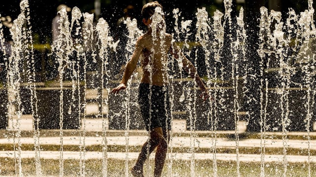 Ein junger Mensch kühlt sich an einem öffentlichen Brunnen im Regierungsviertel von Berlin ab.