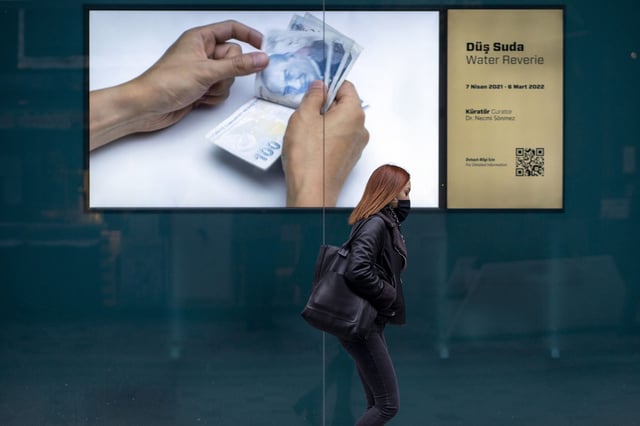 A pedestrian walks by an advertisement showing Turkish lira banknotes on Istiklal Street in Istanbul, Turkey on December 20, 2021.