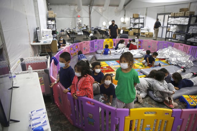In this March 30, 2021, file photo, young unaccompanied migrants, watch television inside a playpen at the U.S. Customs and Border Protection facility, the main detention center for unaccompanied children in the Rio Grande Valley, in Donna, Texas.