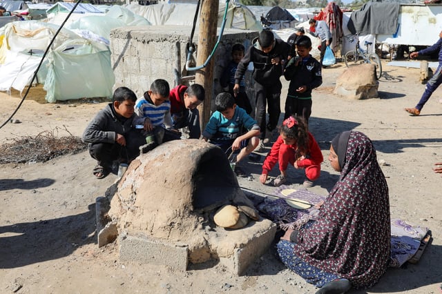 A Palestinian woman bakes bread as children sit next to her, while Gaza residents face crisis levels of hunger and soaring malnutrition, in Khan Younis in the southern Gaza Strip January 24, 2024. REUTERS/Arafat Barbakh/File Photo
