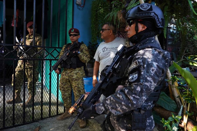 La policía y los soldados se detienen a preguntar a los vecinos sobre una casa vacía mientras patrullan el barrio de San Bartolo en El Salvador, el jueves 17 de julio de 2025. (AP Foto/Salvador Melendez)