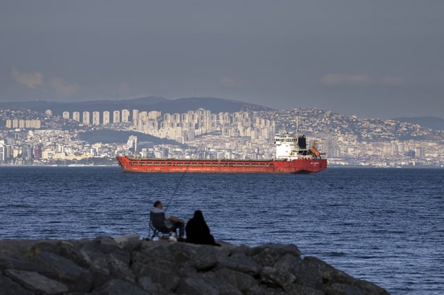 A family sit on a rock in front of a cargo ship anchors in the Marmara Sea awaits to access to cross the Bosphorus Straits in Istanbul, Turkey, on July 13, 2022.