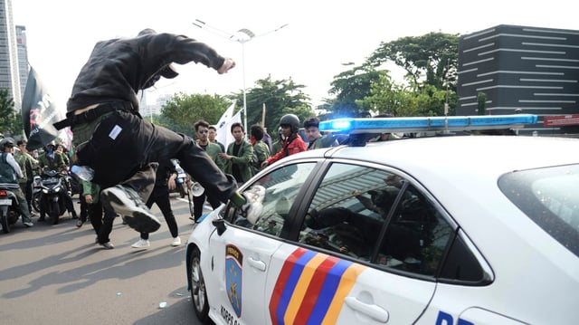 A student attacks a police car during a protest in Jakarta after the death of a motorcycle rider, who was run over by a police armoured vehicle