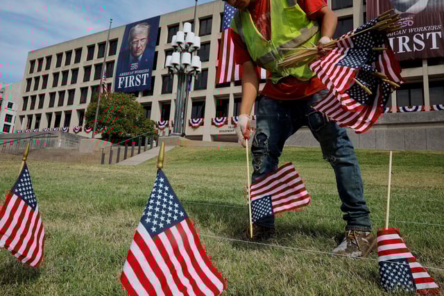 A worker plants US flags in front of the Department of Labor building, from which hangs a giant banner of President Donald Trump, in Washington, DC, on August 28.