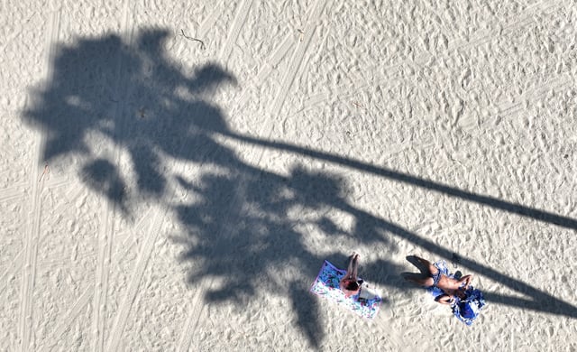 Long Beach, CA – August 21: A couple relax on the beach in the shade of palm trees to beat the heat amid a heat wave in SoCal in Long Beach Thursday, Aug. 21, 2025.  (Allen J. Schaben / Los Angeles Times via Getty Images)