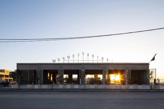 Western facade at sunrise. Decorative elements are minimal, consisting primarily of spinning stainless-steel letters on the roof acting as a weathervane.