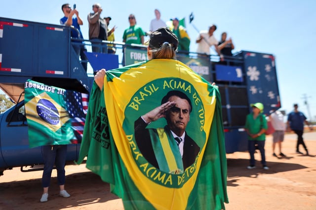 A person wears a flag with a picture of former Brazilian President Jair Bolsonaro, as supporters of the former president gather outside his condominium complex where he is under house arrest, waiting for the last instance of his trial accused of plotting a coup after his electoral defeat in Brasilia, Brazil August 31, 2025. REUTERS/Jorge Silva